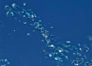 Close-up of small water droplets suspended in the air against a deep blue background, capturing the sparkling and translucent quality of the water.