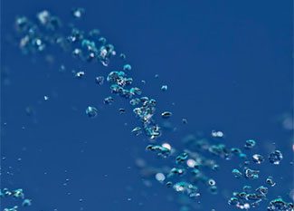 Small water droplets are suspended in mid-air against a deep blue background, creating a sparkling, dynamic effect.