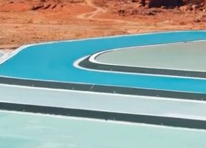 Aerial view of a winding series of bright blue and pale green evaporation ponds set against a dry, reddish-brown desert landscape.
