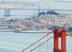 View of San Francisco with the top of the Golden Gate Bridge in the foreground, city buildings, water, and another bridge visible in the background—featured in a recent Capcomm Partners website study.