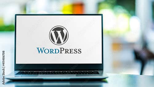 A laptop displaying the WordPress logo and text on its screen, set against a blurred background with green, yellow, and white tones.